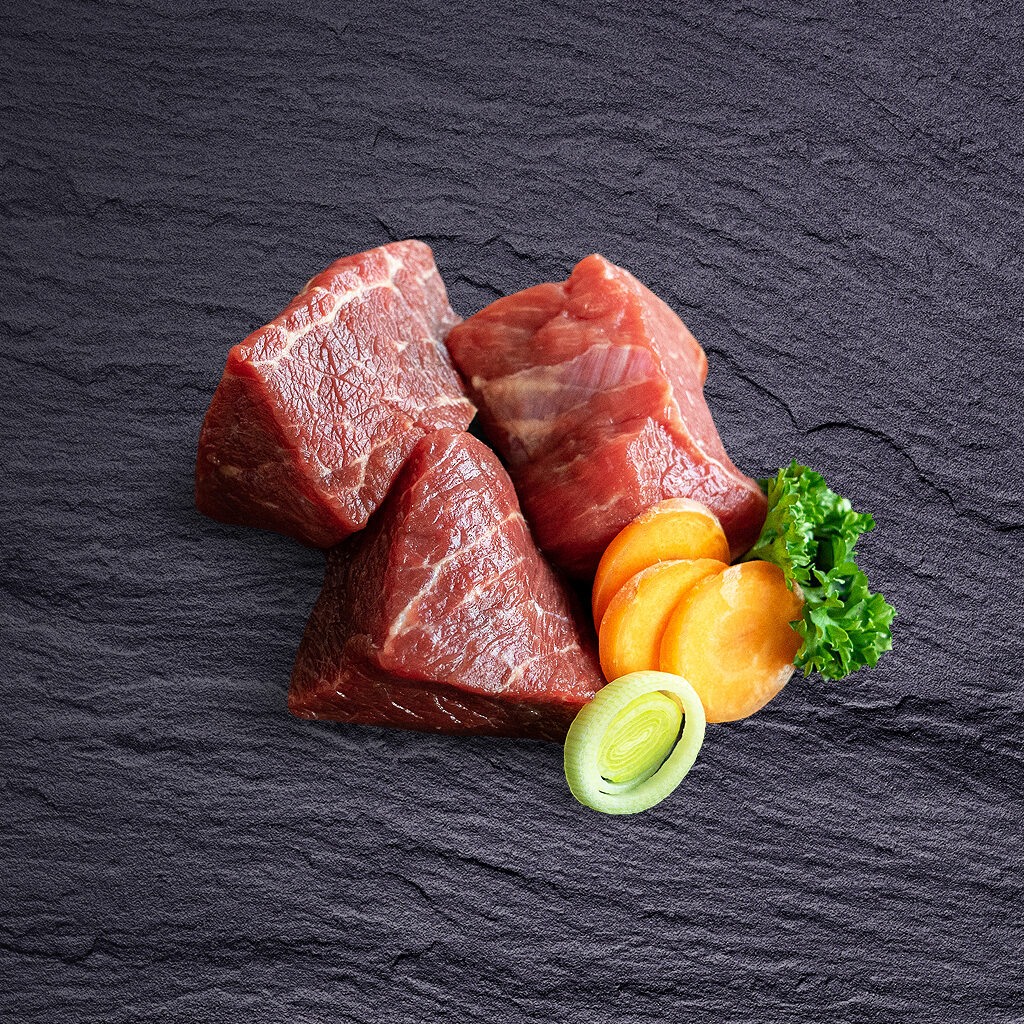 Frisches Rindergulasch aus hochwertigem Rindfleisch auf dunkler Schieferplatte mit Lauch, Karotten und Petersilie